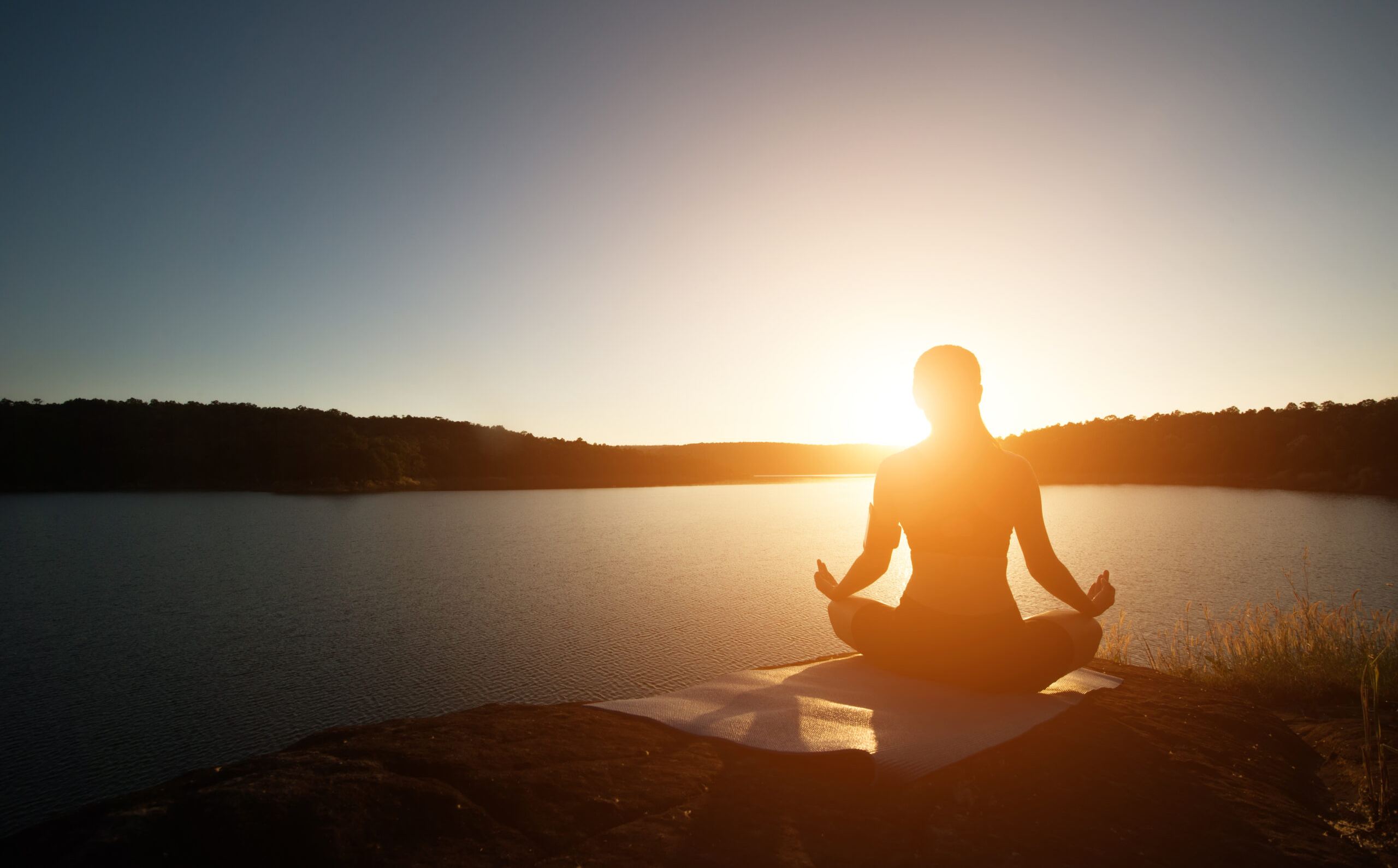 Silhouette of woman is practicing yoga at mountain lake